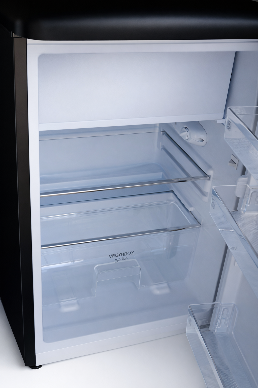 Interior view of an empty refrigerator with glass shelves and a veggie drawer.