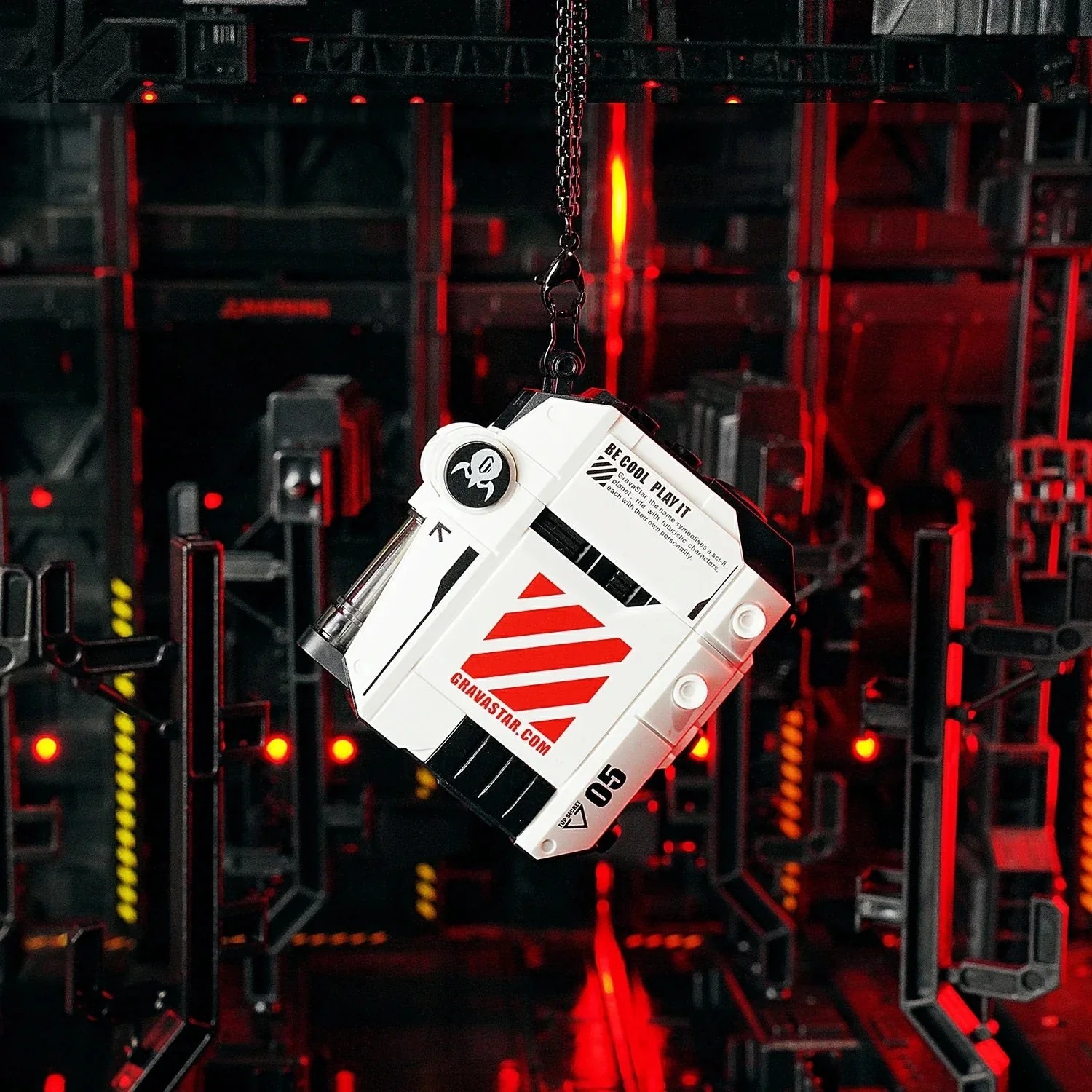 Biały, futurystyczny głośnik z czerwonymi paskami wisi na łańcuchu na ciemnym, podświetlonym na czerwono tle.