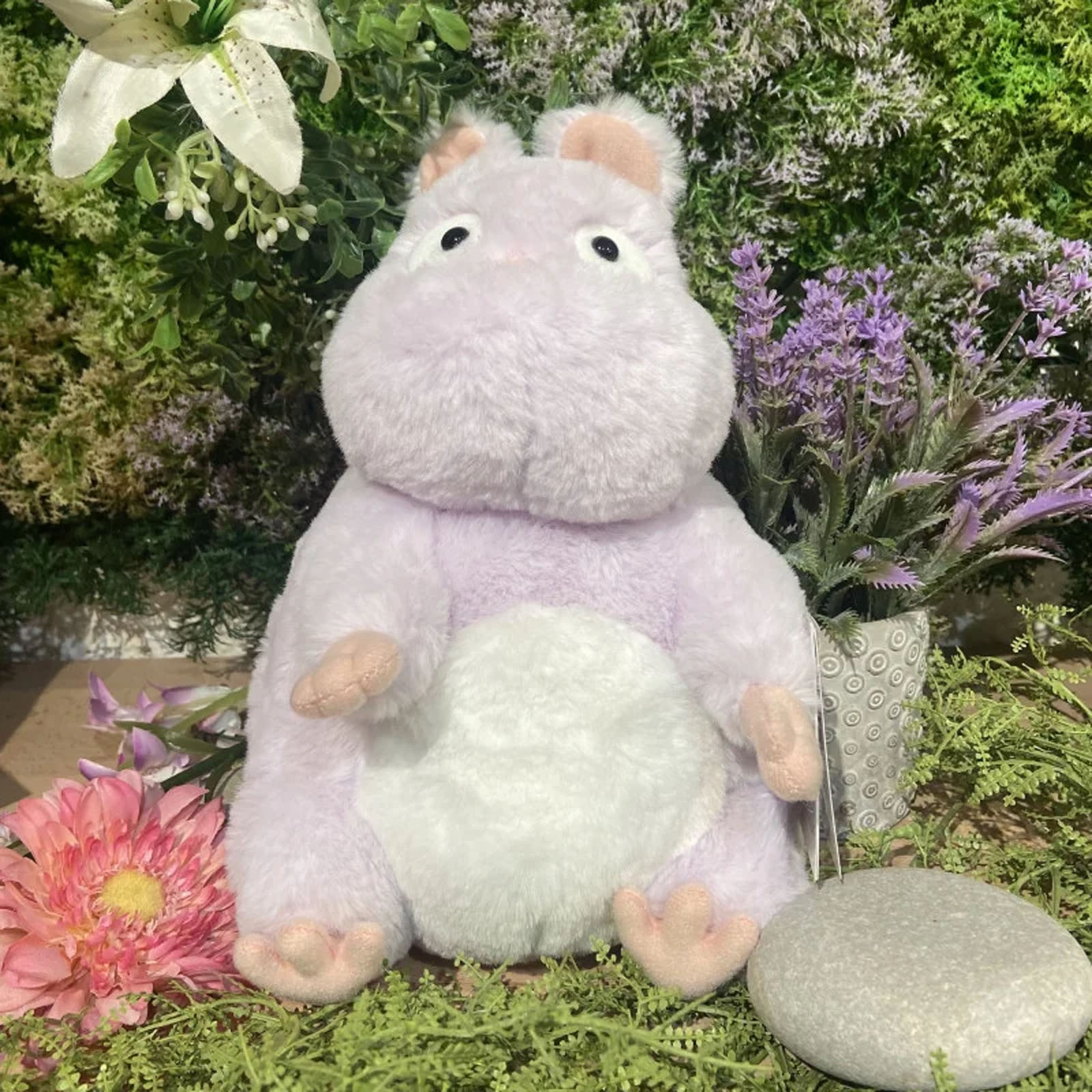 Ein lilafarbener Plüschteddy sitzt inmitten von Blumen und Grünzeug.