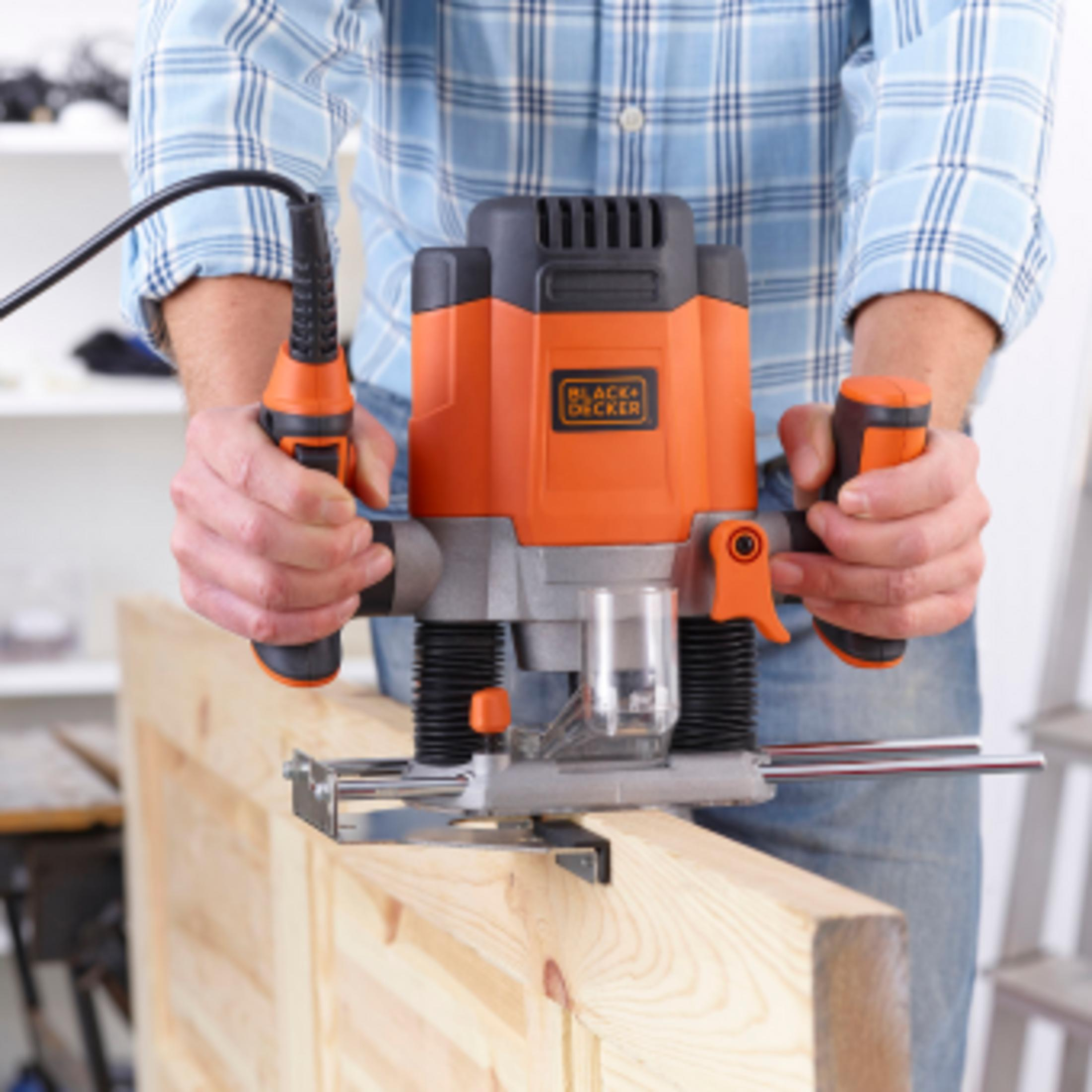 Una persona con camisa a cuadros usa una fresadora manual naranja en una tabla de madera.