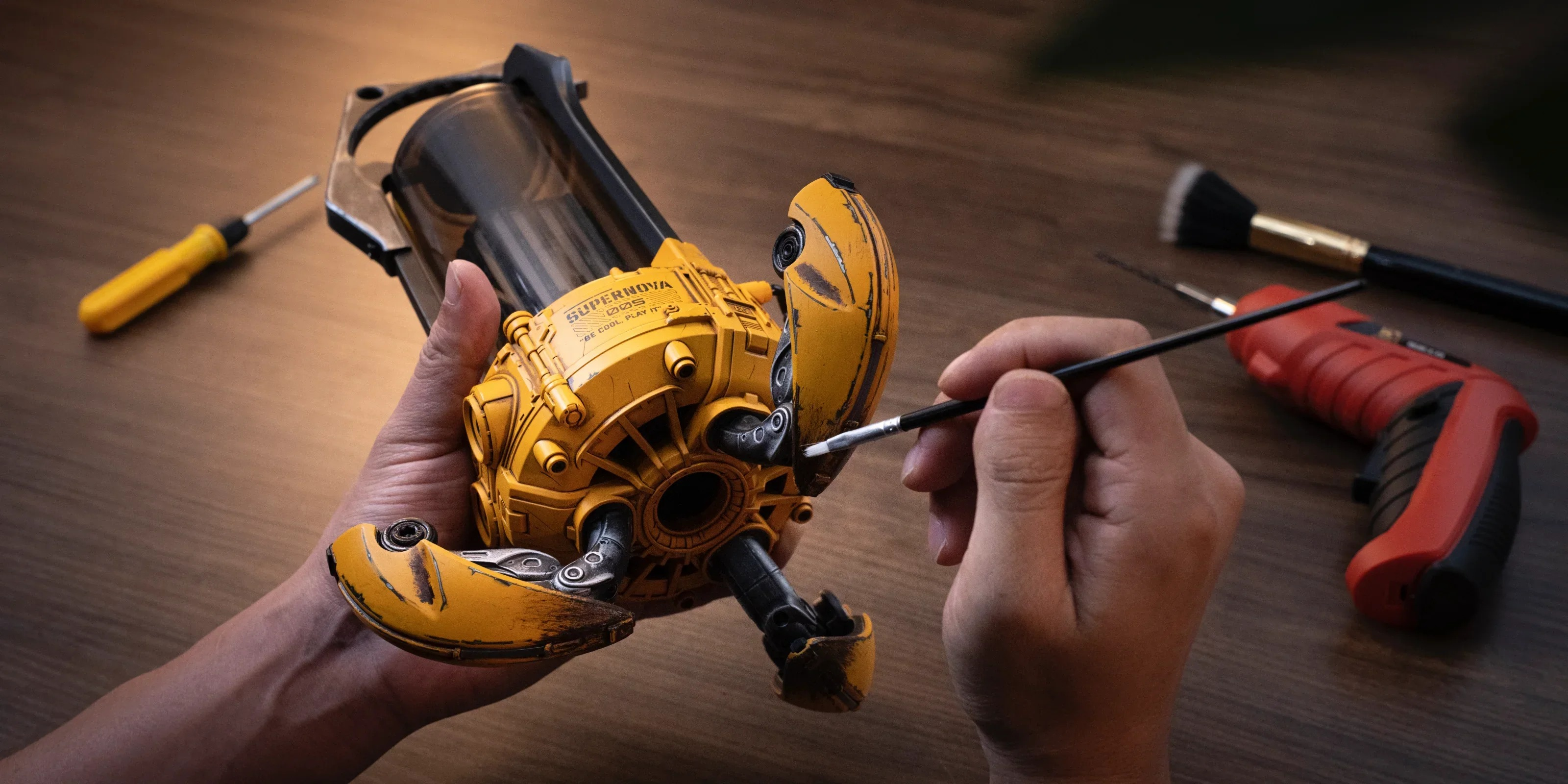 Dłonie malują pędzlem żółty model robota. Narzędzia leżą w pobliżu.