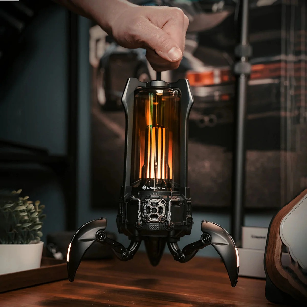 Ręka trzyma futurystyczną lampę z nogami i pomarańczowym światłem.