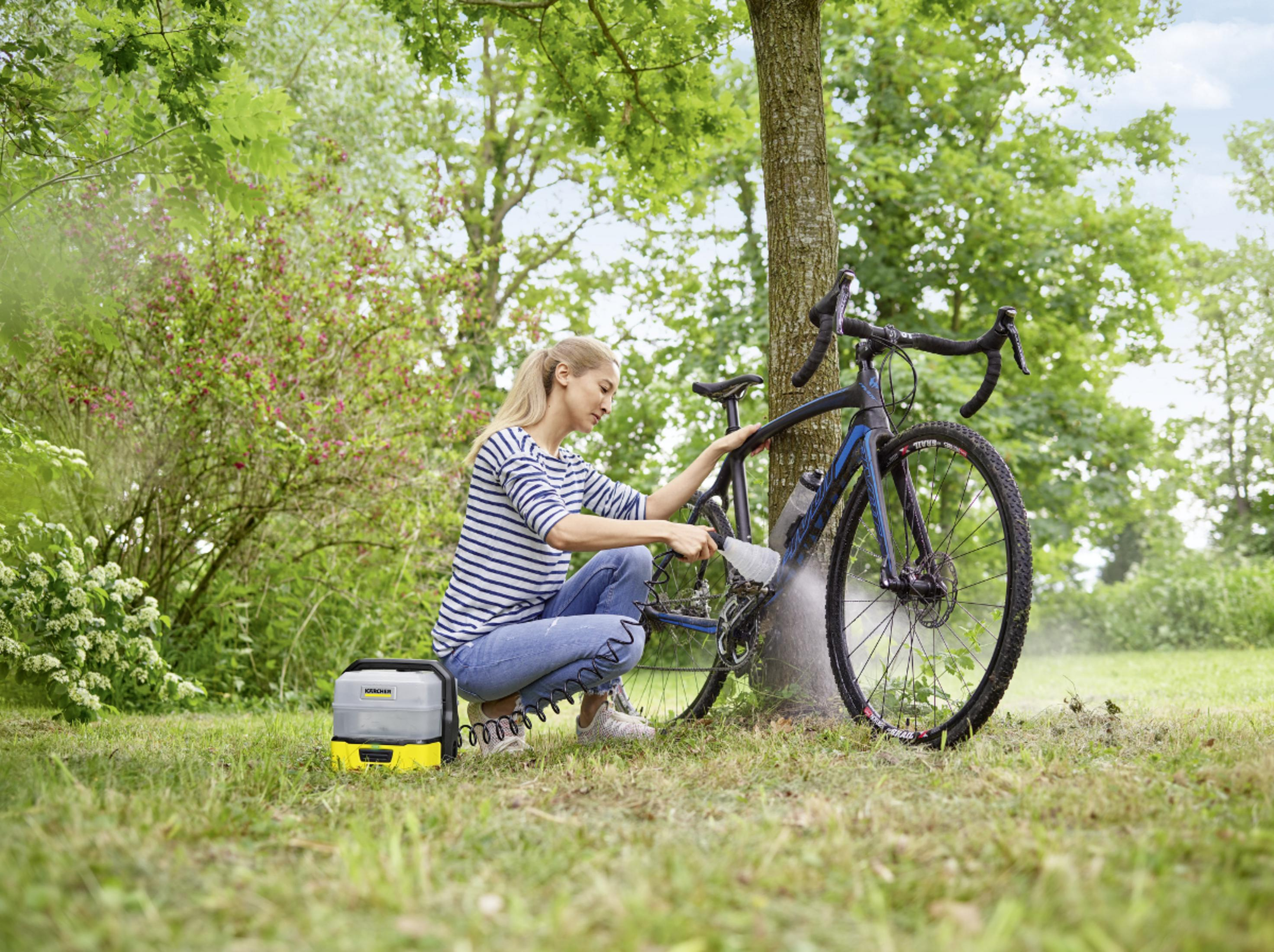 Donna pulisce bicicletta con idropulitrice all'aperto vicino a un albero.