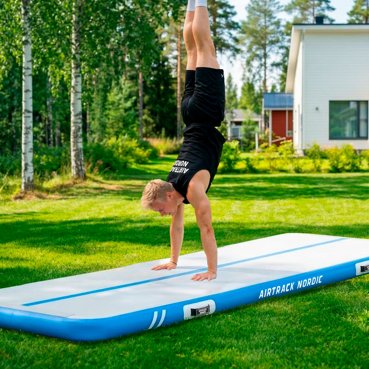 Mężczyzna wykonuje stanie na rękach na niebieskiej macie airtrack na trawie na zewnątrz.