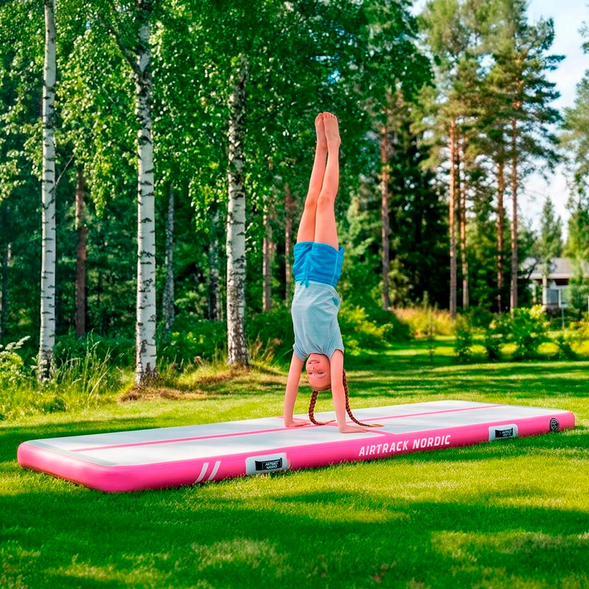 Dziewczynka robi stanie na rękach na dmuchanej macie gimnastycznej na zewnątrz, wśród drzew.