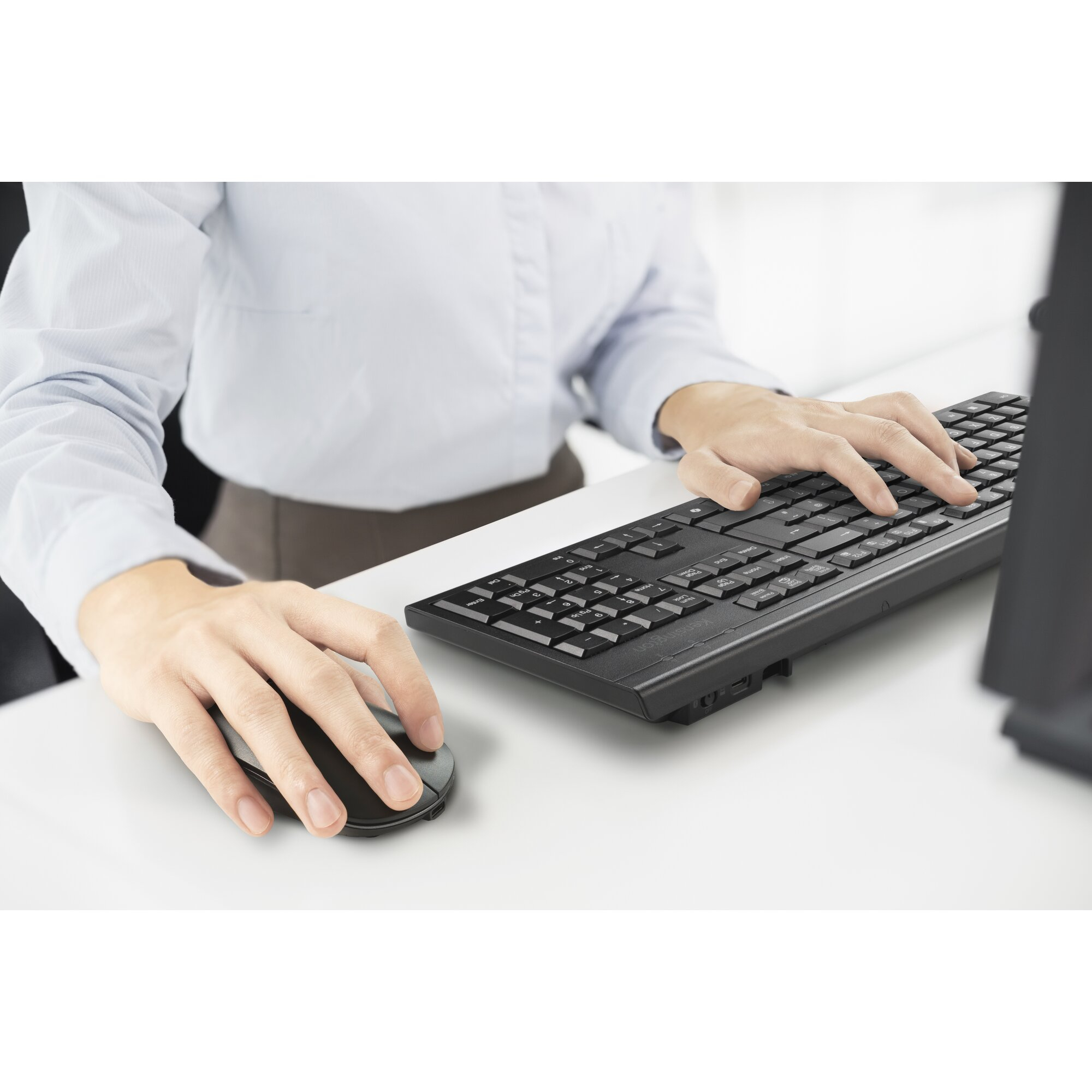 Person in blauem Hemd benutzt schwarze Tastatur und Maus auf weißem Schreibtisch.