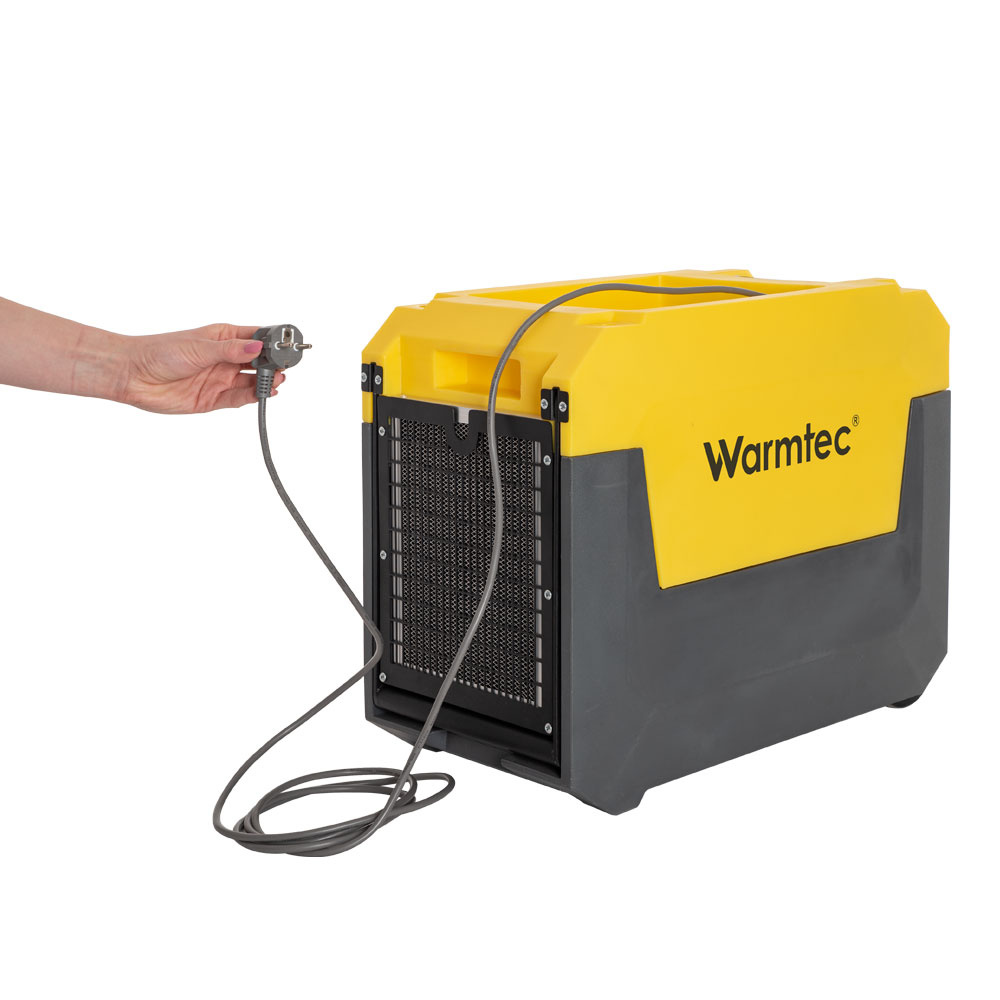 Ręka trzyma wtyczkę podłączoną do żółto-szarego urządzenia Warmtec.