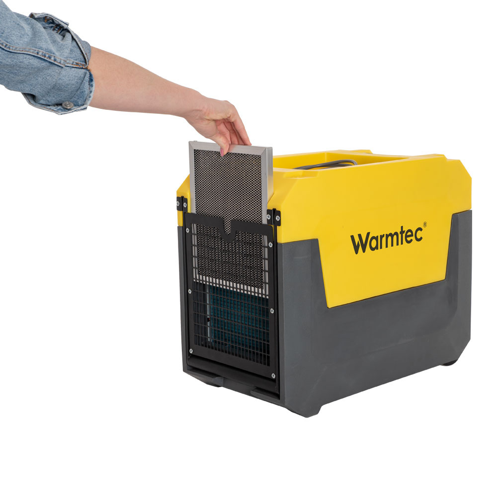 Dłoń w dżinsowym rękawie wkłada filtr do żółto-szarego urządzenia Warmtec.