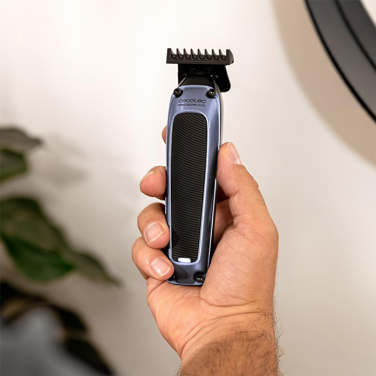 Una mano sujeta una recortadora de pelo azul con mango negro y accesorio de peine.