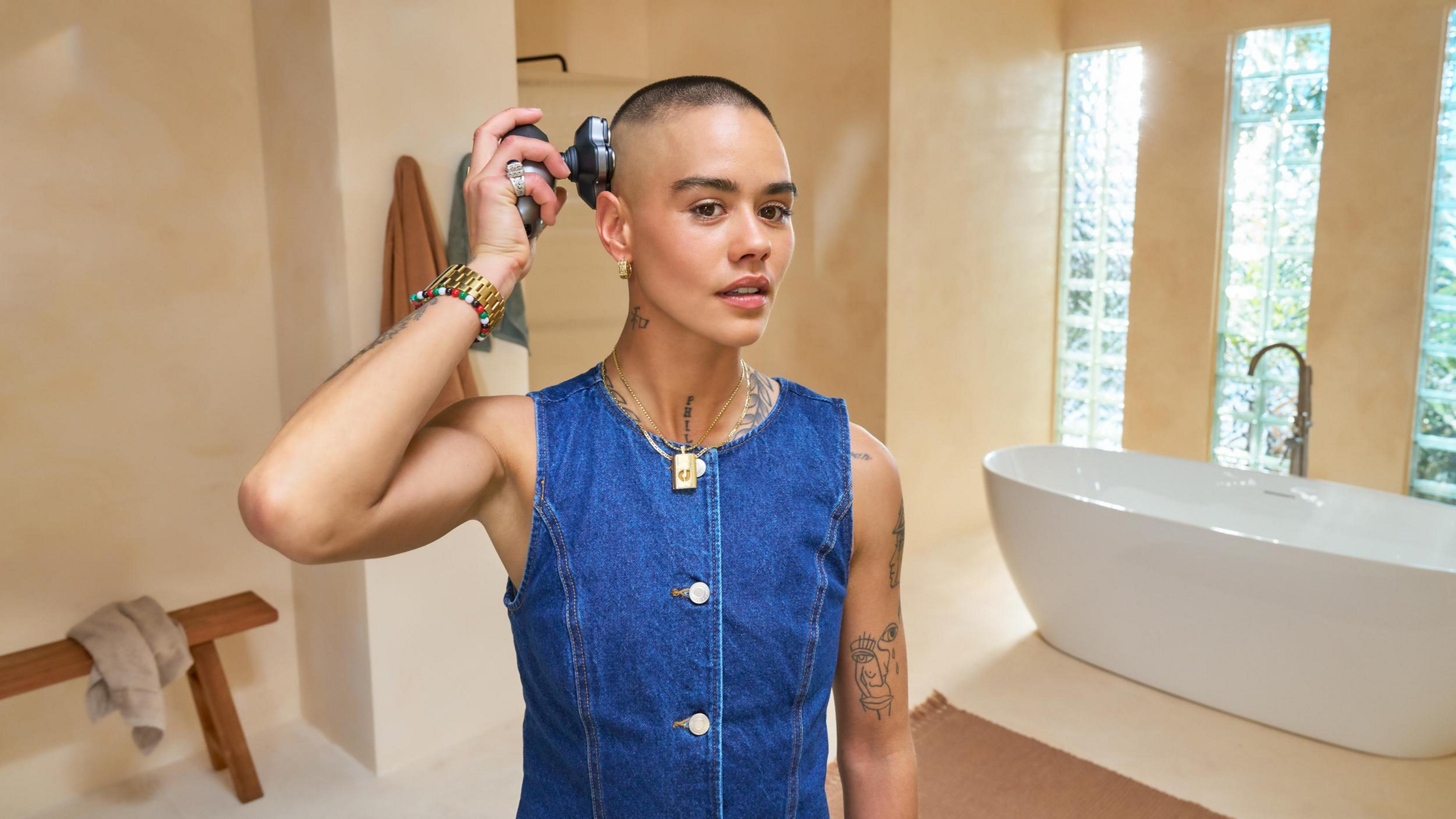 Persona si rade la testa in bagno con vasca e panca di legno.