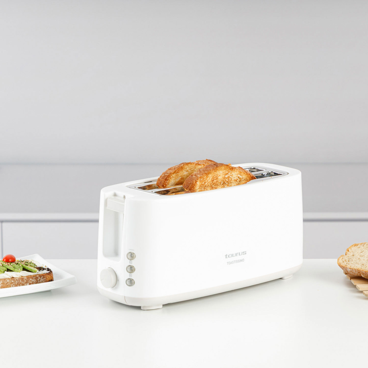 Un tostapane bianco con due fette di pane tostato, accanto un panino.