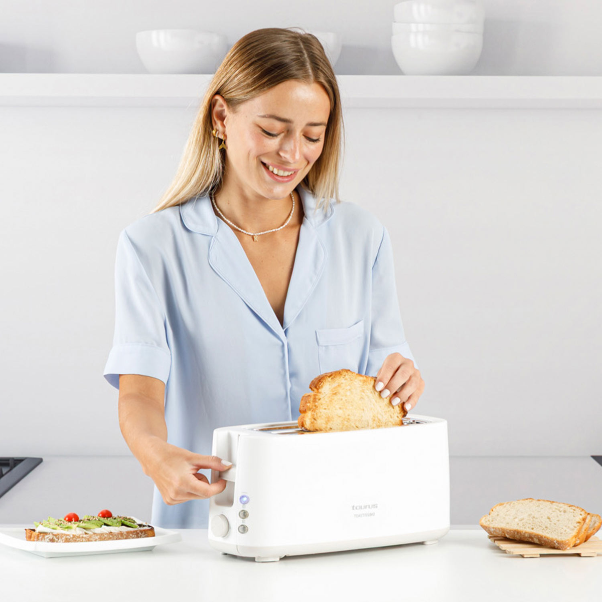 Una donna mette il pane nel tostapane bianco. Sul tavolo c'è una fetta di pane condita.