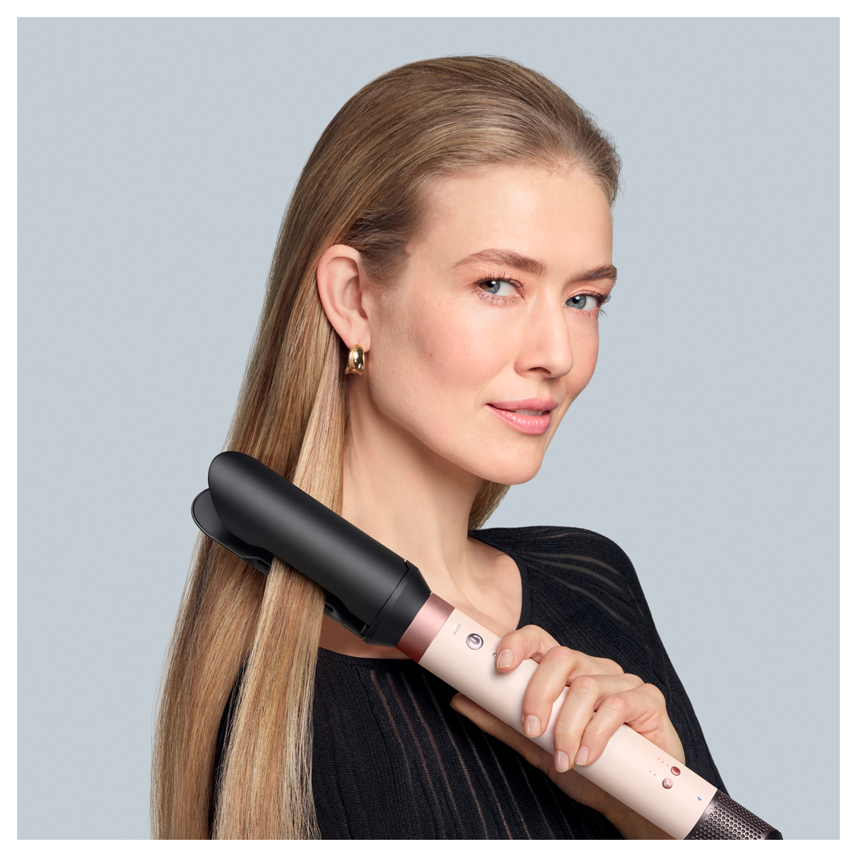 Una donna con i capelli biondi tiene un ferro arricciacapelli.