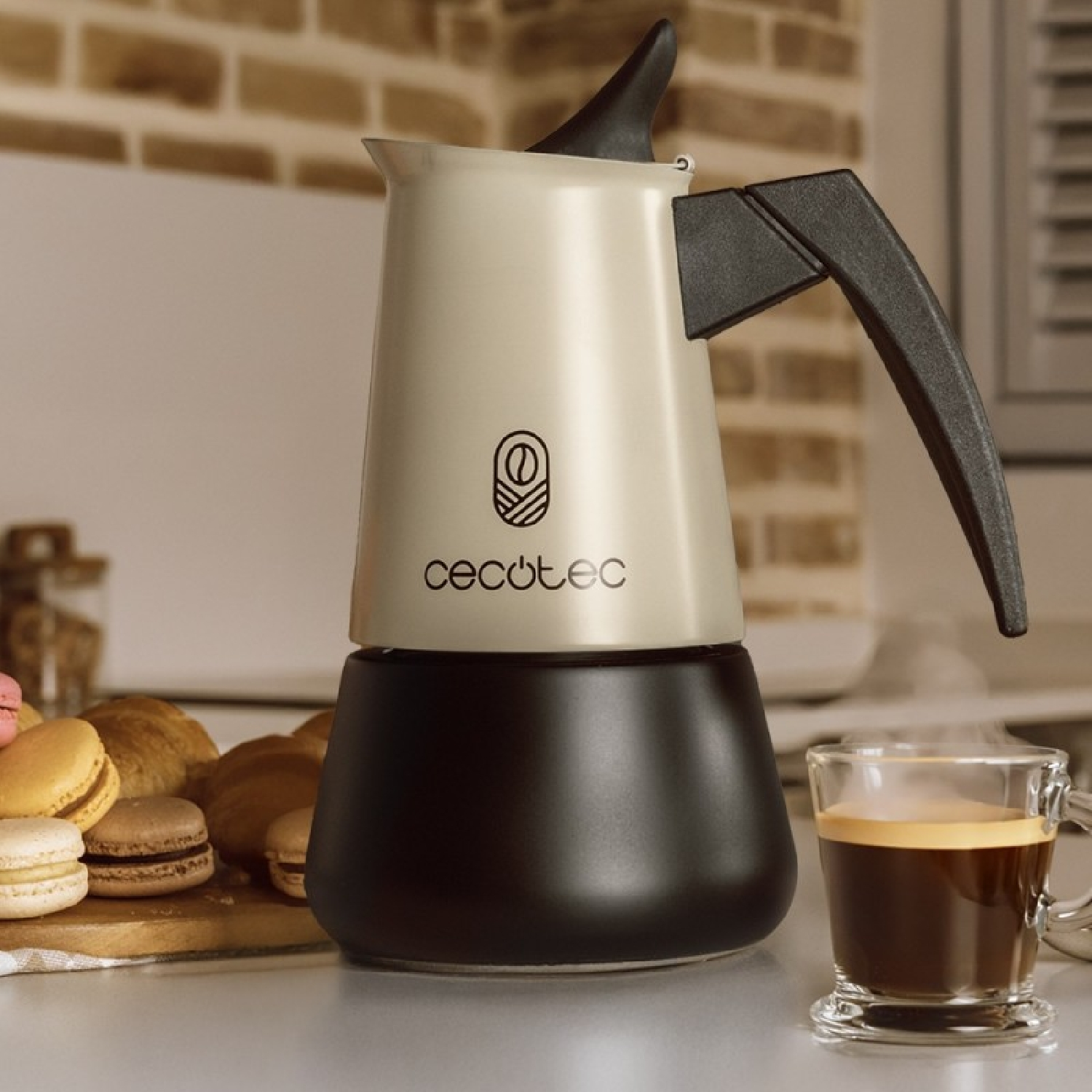 Una caffettiera beige e nera accanto a una tazza di espresso in vetro e pasticcini.