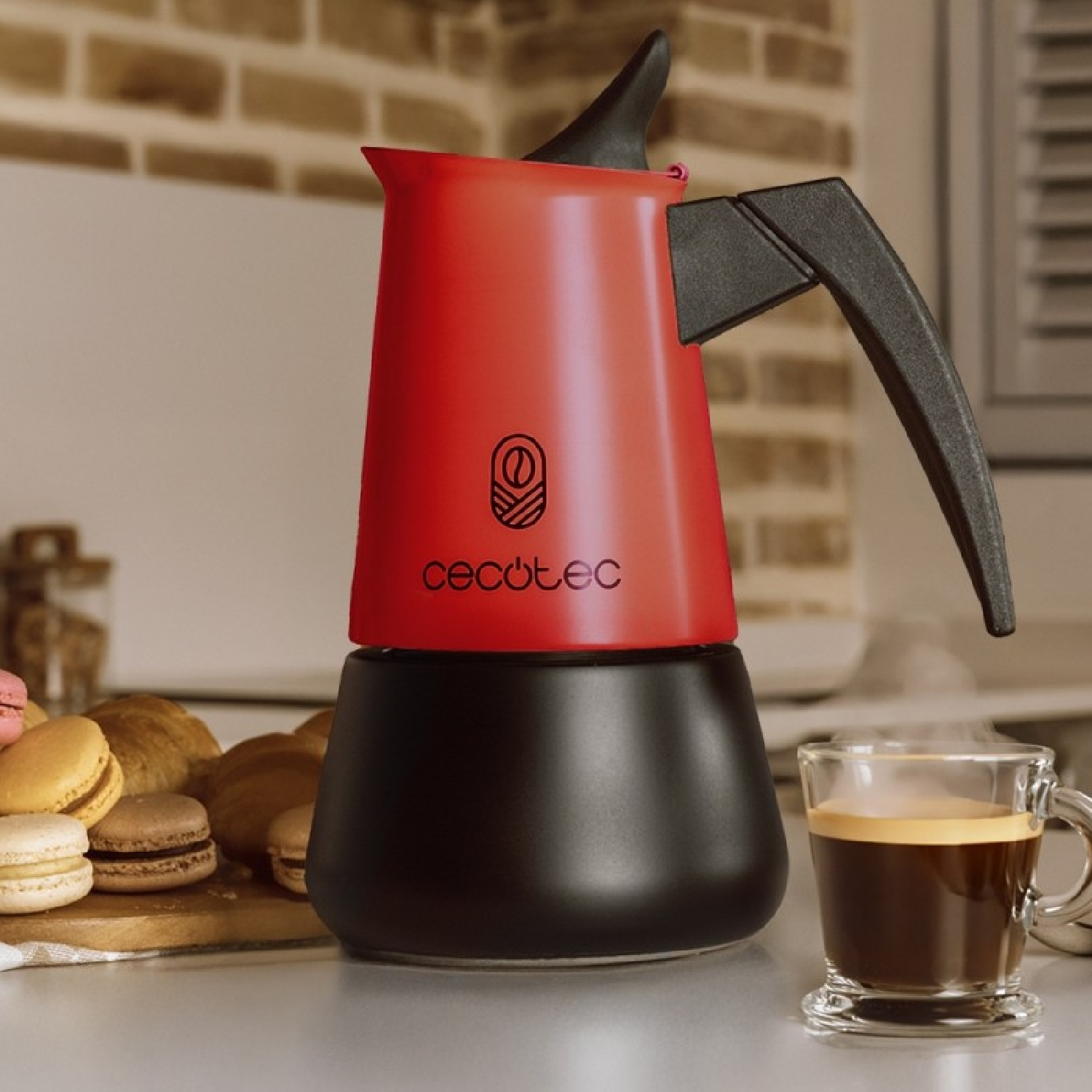 Una caffettiera rossa con base nera, pasticcini e un espresso accanto.