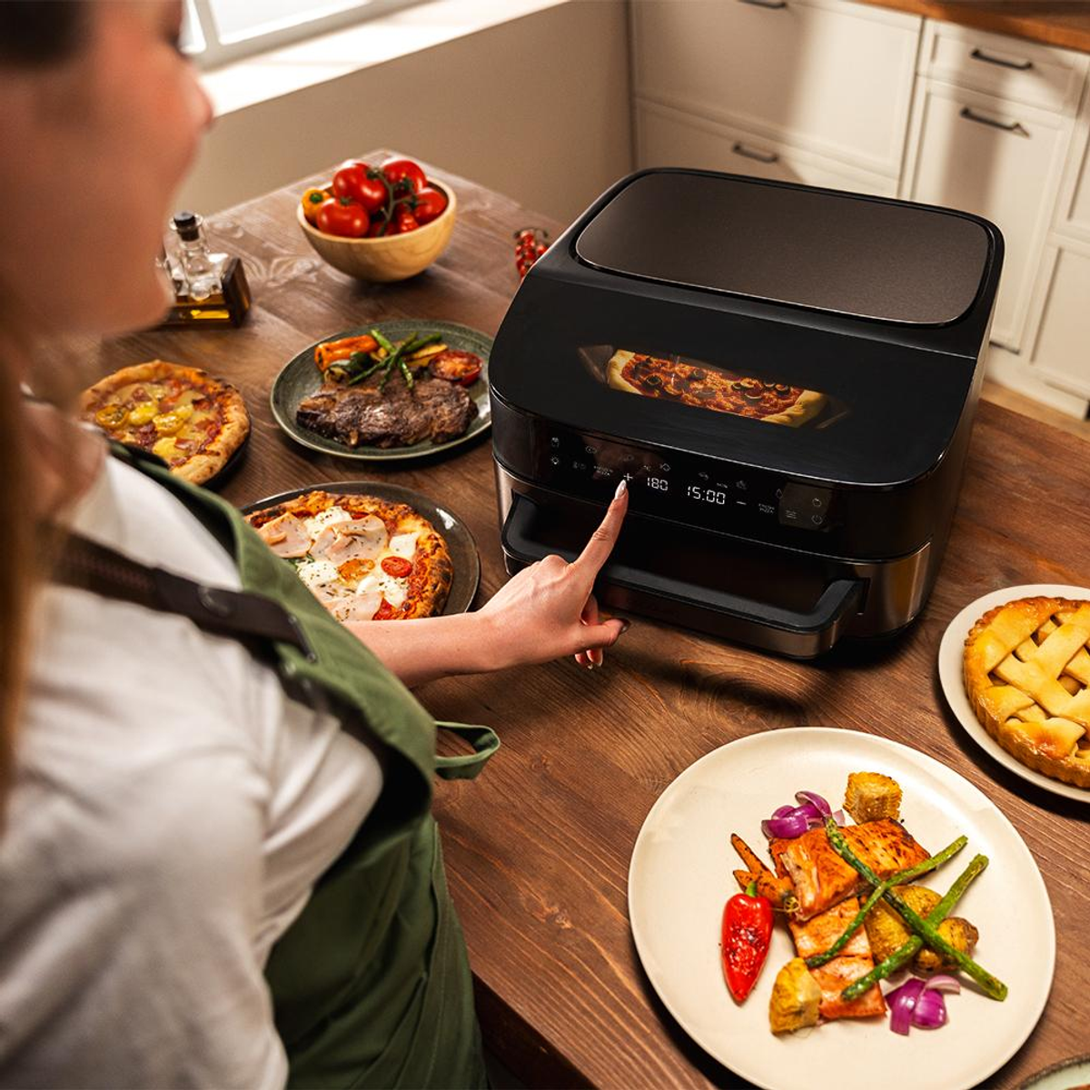 Una persona usa una friggitrice ad aria nera con display pizza, cibo accanto.