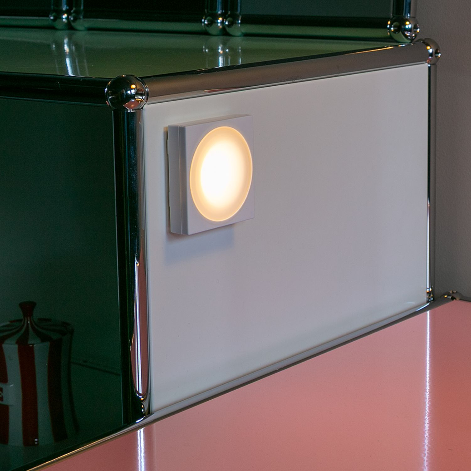 Ein quadratisches Licht beleuchtet eine weiße Oberfläche eines Modulschranks mit Chromleisten.