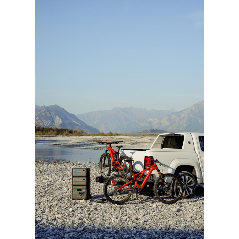 Weißer Pickup mit zwei orangen Fahrrädern auf einem Träger, an einem Fluss.