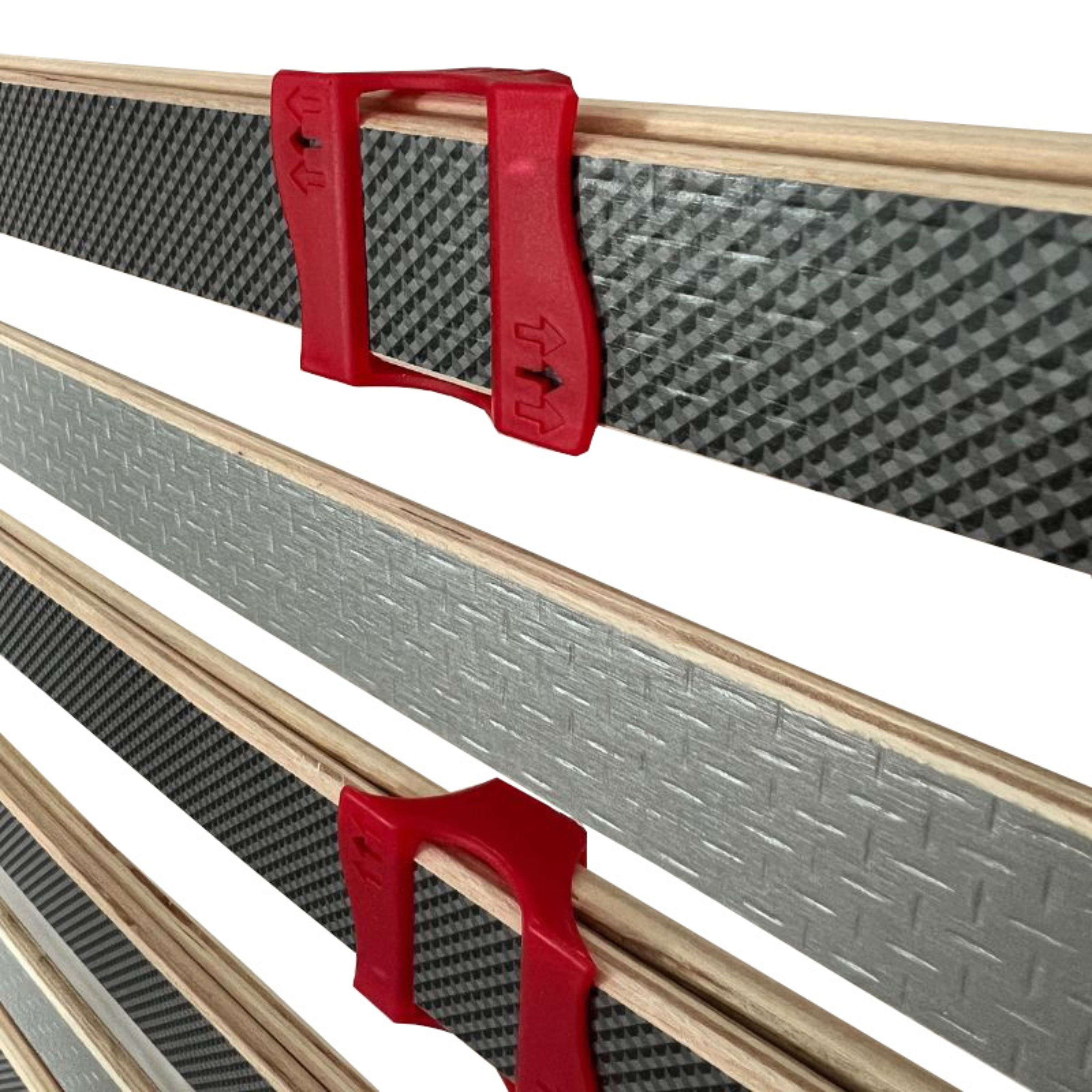 Dos clips rojos sujetan listones de madera con patrones sobre fondo blanco.