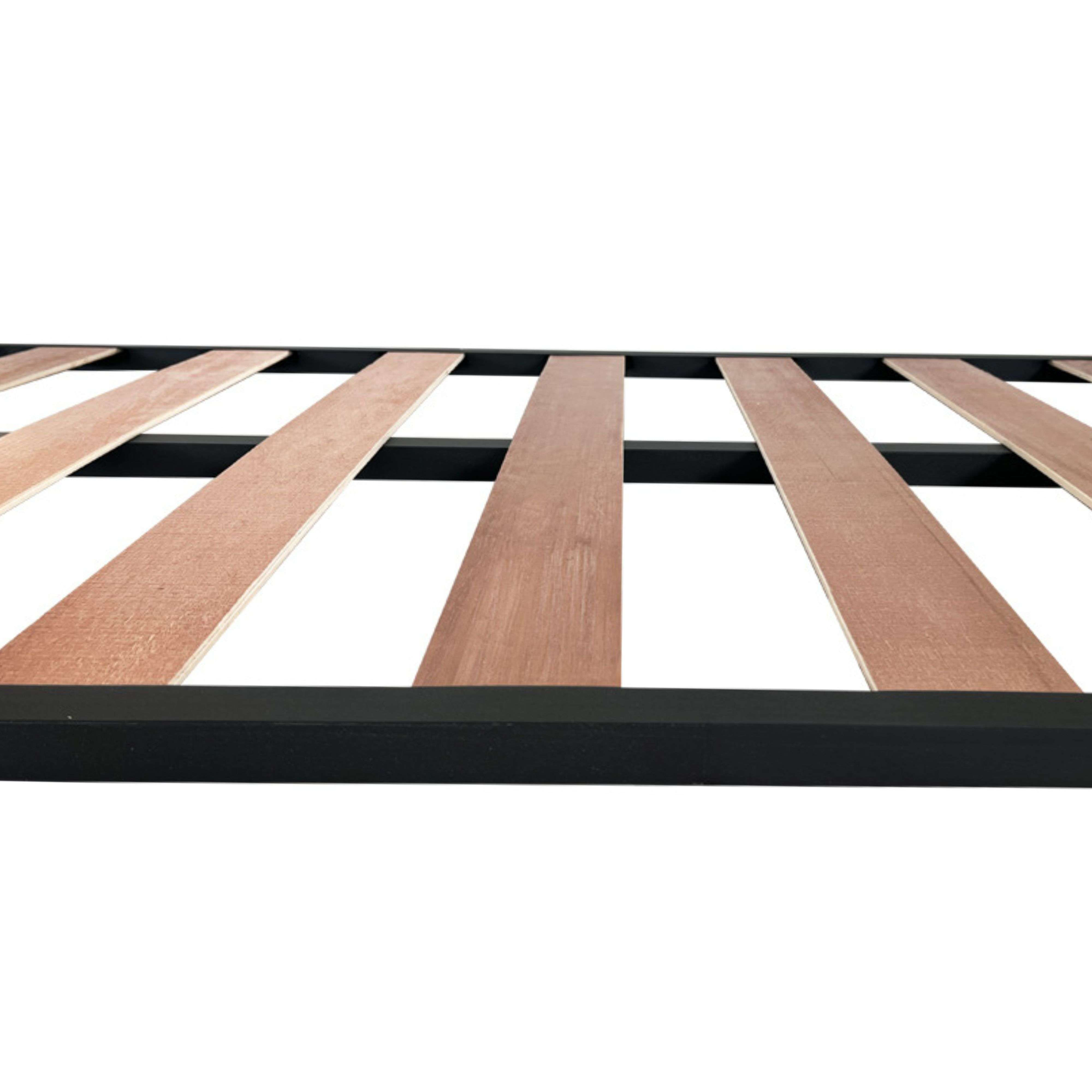 Un somier con listones de madera y marco metálico negro, visto de cerca.
