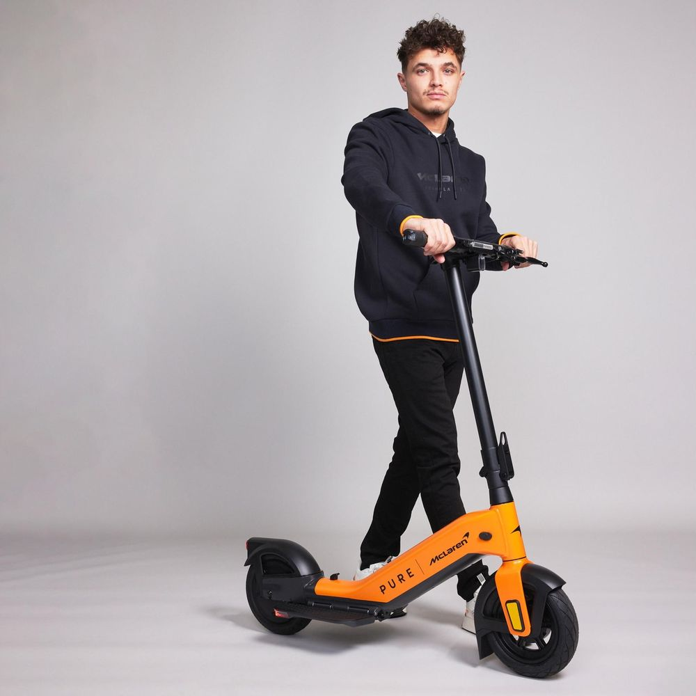 Ein Mann mit lockigen Haaren steht auf einem orangefarbenen Elektroroller.