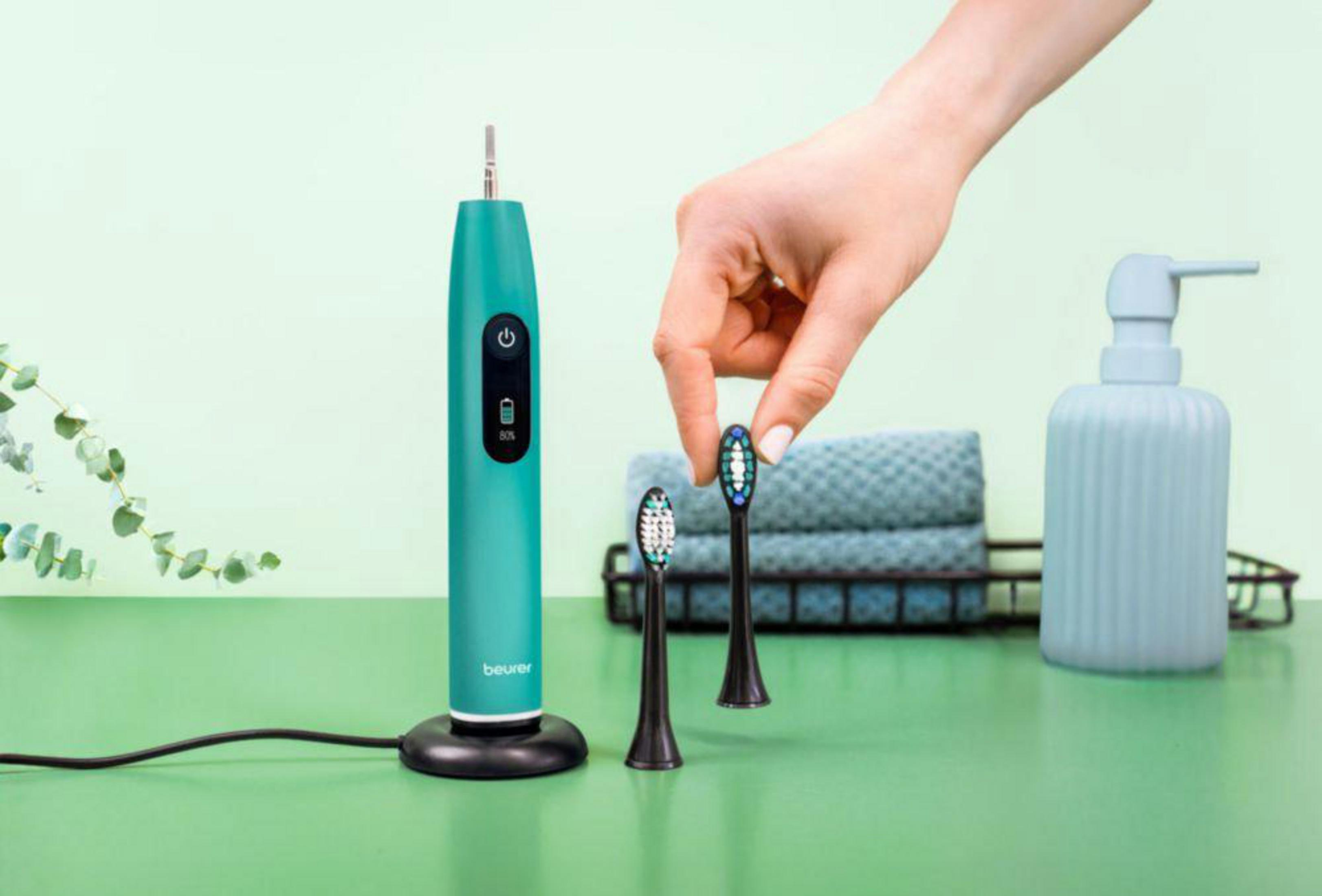 Turquoise elektrische tandenborstel handvat met twee zwarte borstelkoppen en een dispenser.