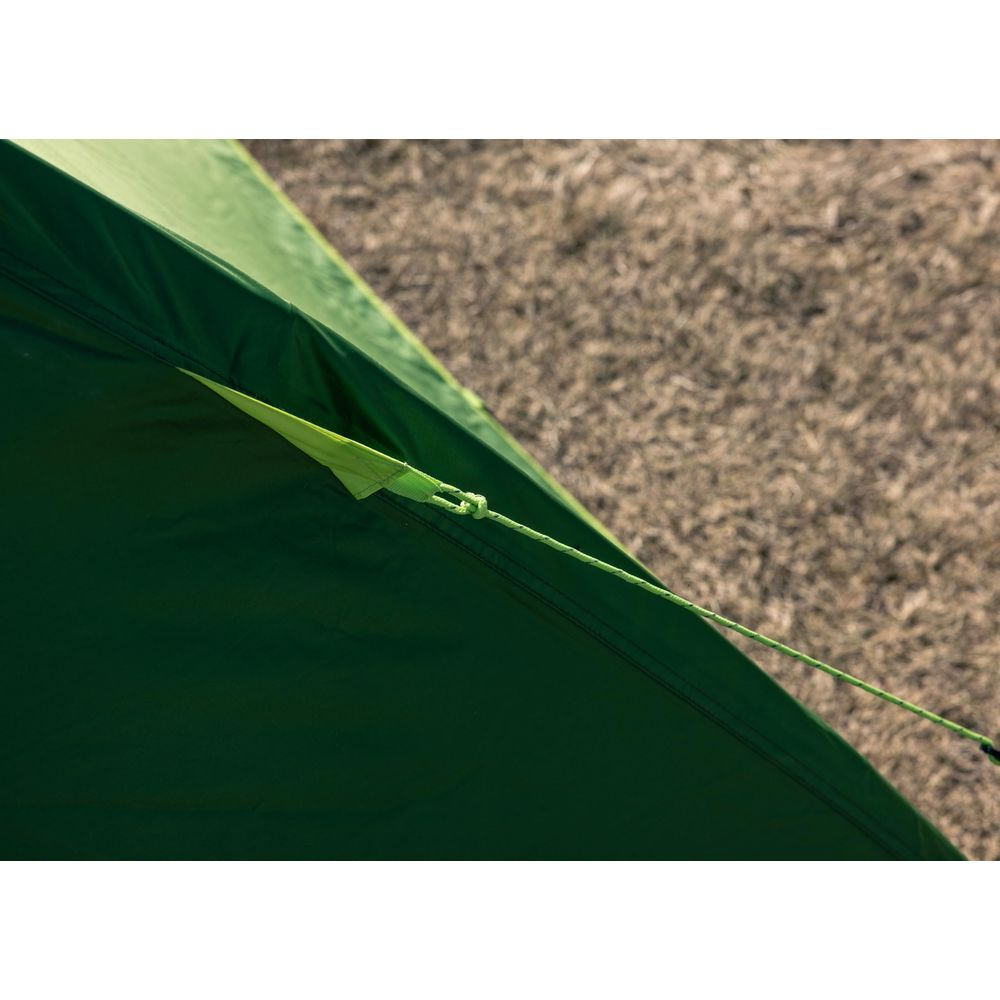 Primo piano di tessuto verde tenda con fissaggio corda su erba secca.