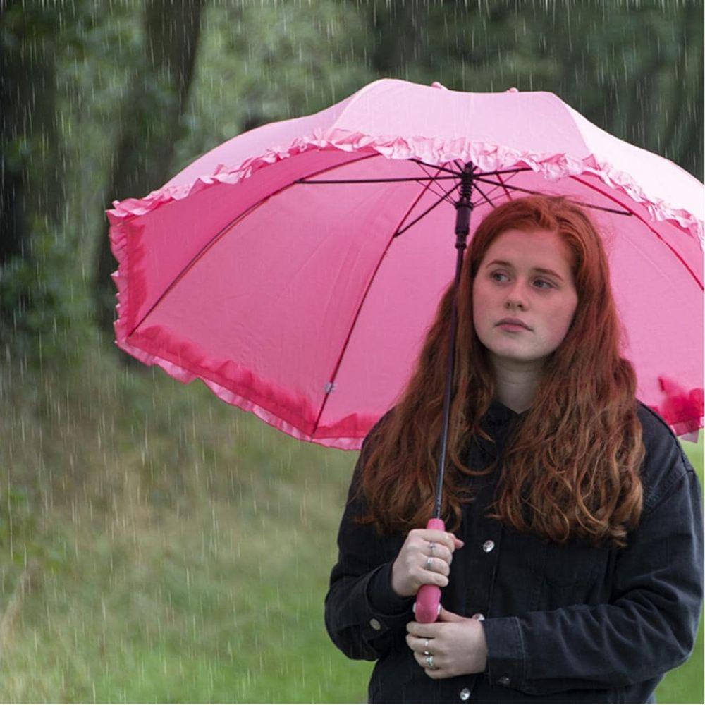 Ein rothaariges Mädchen mit einem rosa Regenschirm im Regen.