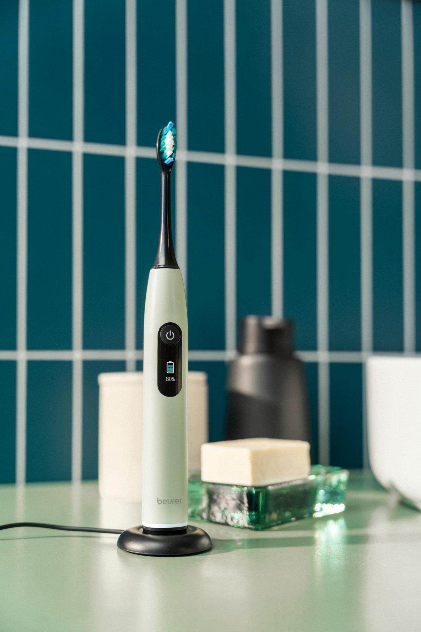 A light green electric toothbrush with a black handle stands on a charging base.