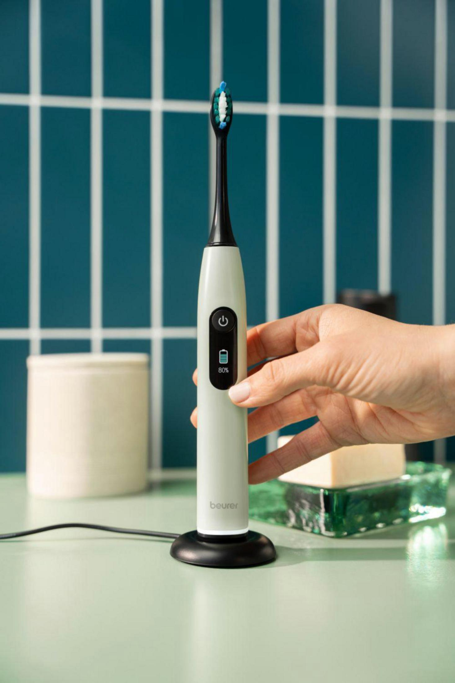 A hand holds an electric toothbrush with blue-green bristles.