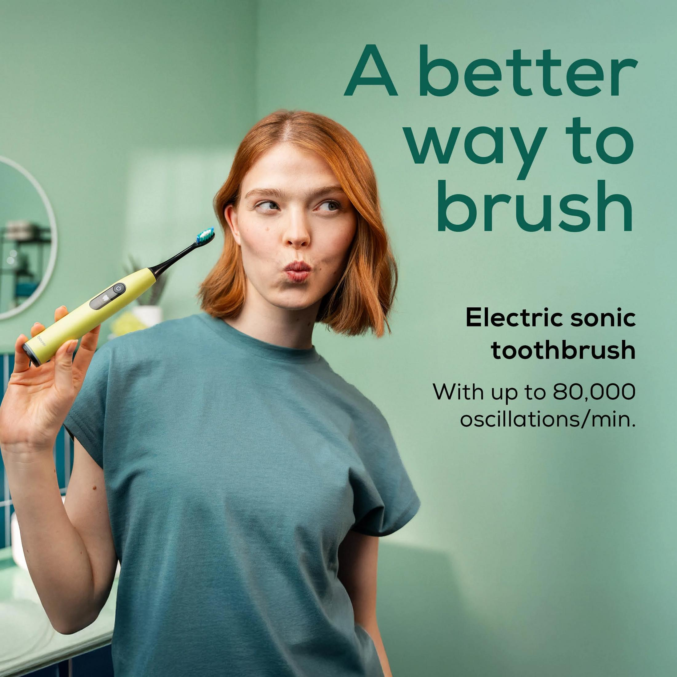 Woman with red hair holds a yellow sonic toothbrush against a mint green background.