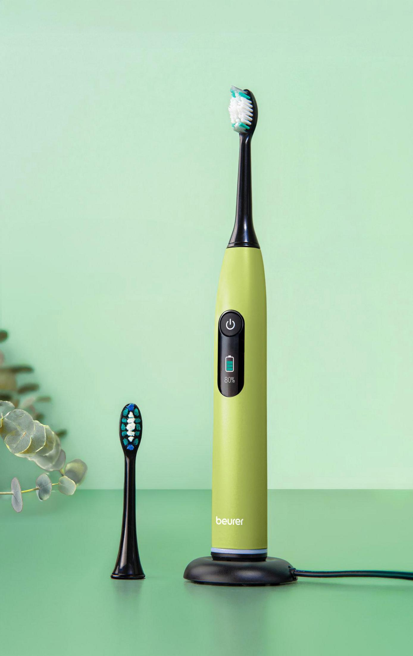 A green electric toothbrush with a black head rests on a charging base.