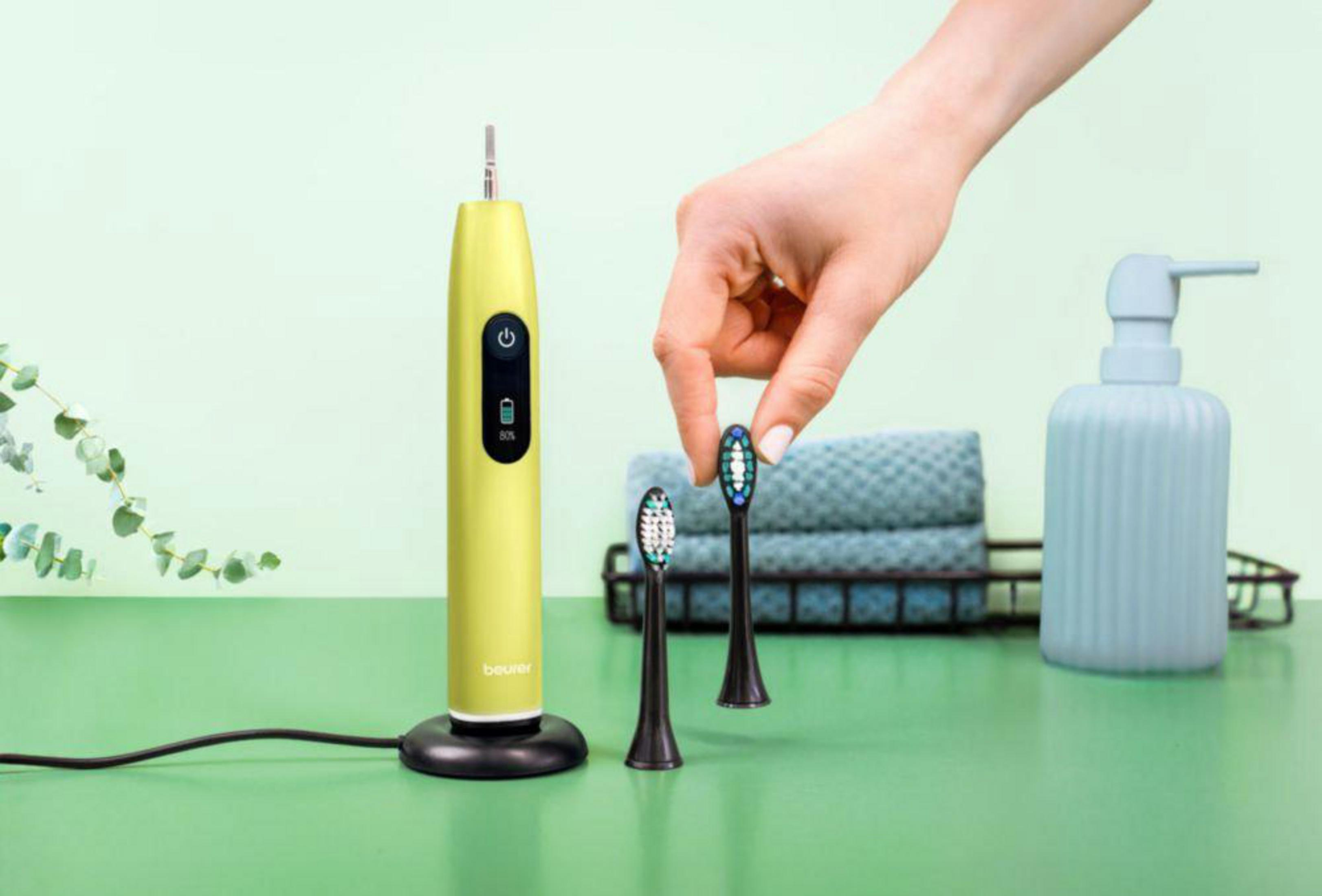 A hand holds a black brush head for a yellow toothbrush.