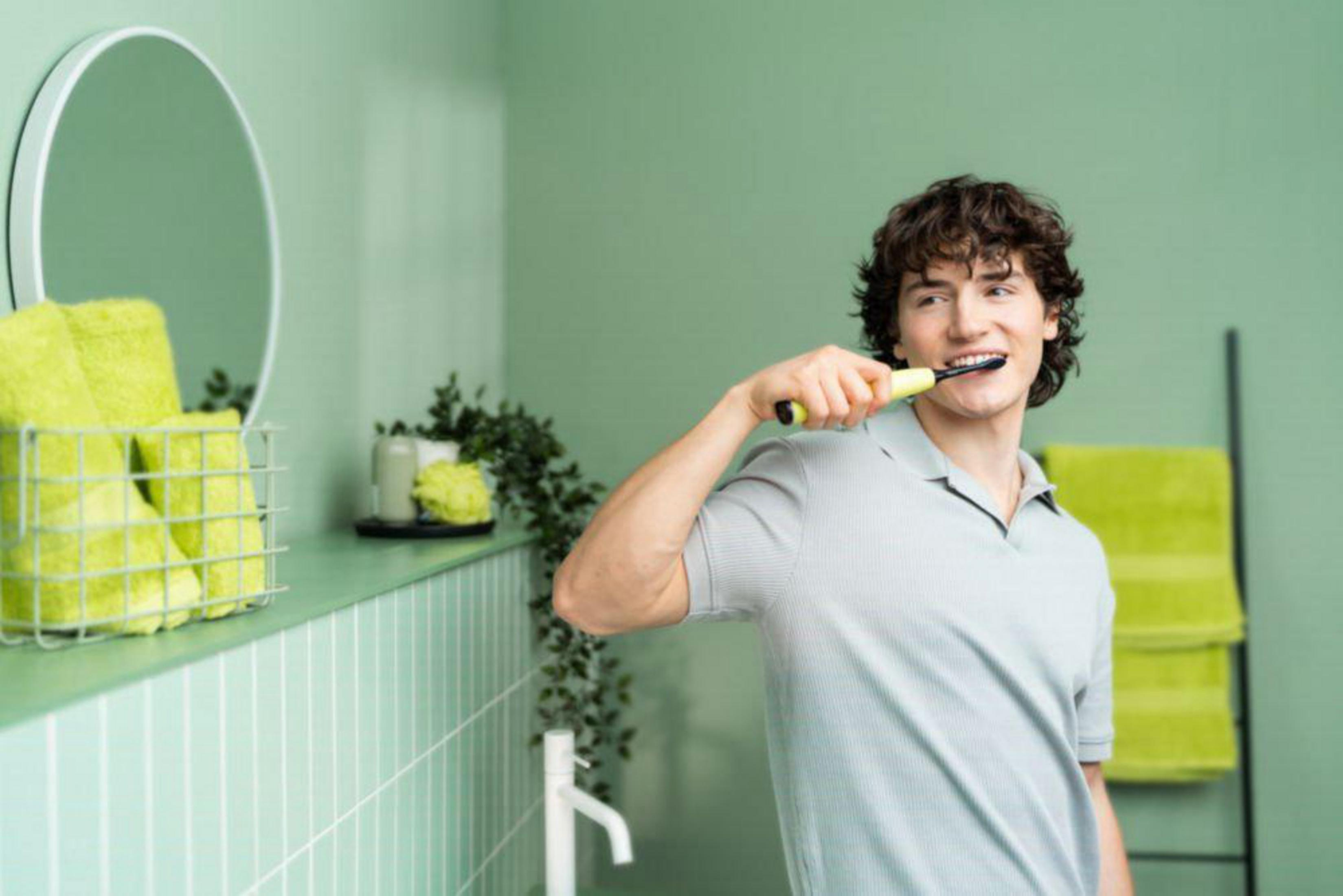 A man brushes his teeth with a yellow toothbrush in a green bathroom.