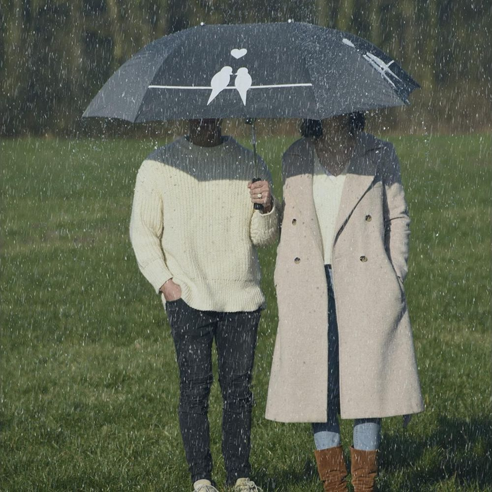 Zwei Personen stehen unter einem Regenschirm mit Vogelmotiv im Regen.