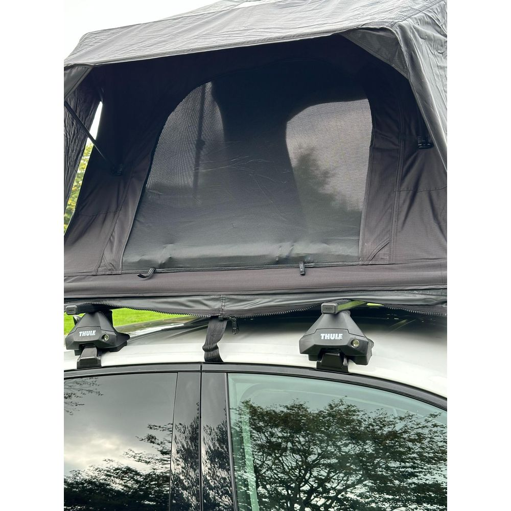 Una tenda da tetto è montata su un'auto bianca con portapacchi Thule.