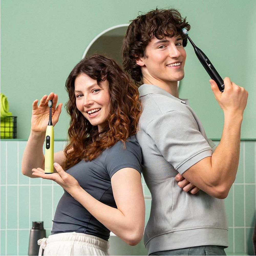 Man and woman stand back to back holding toothbrushes.