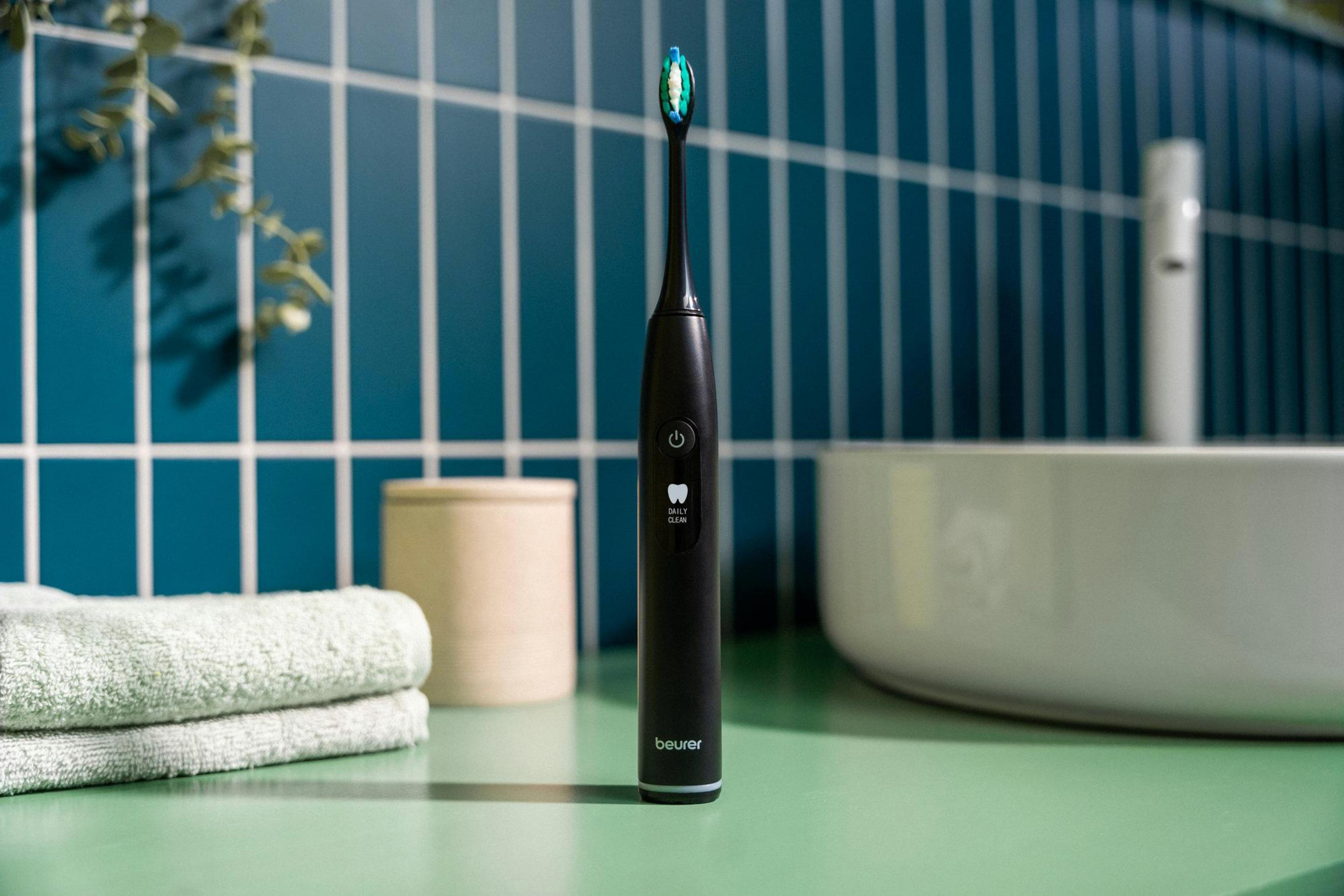 Black electric toothbrush with blue-green bristles, towels, and cup.