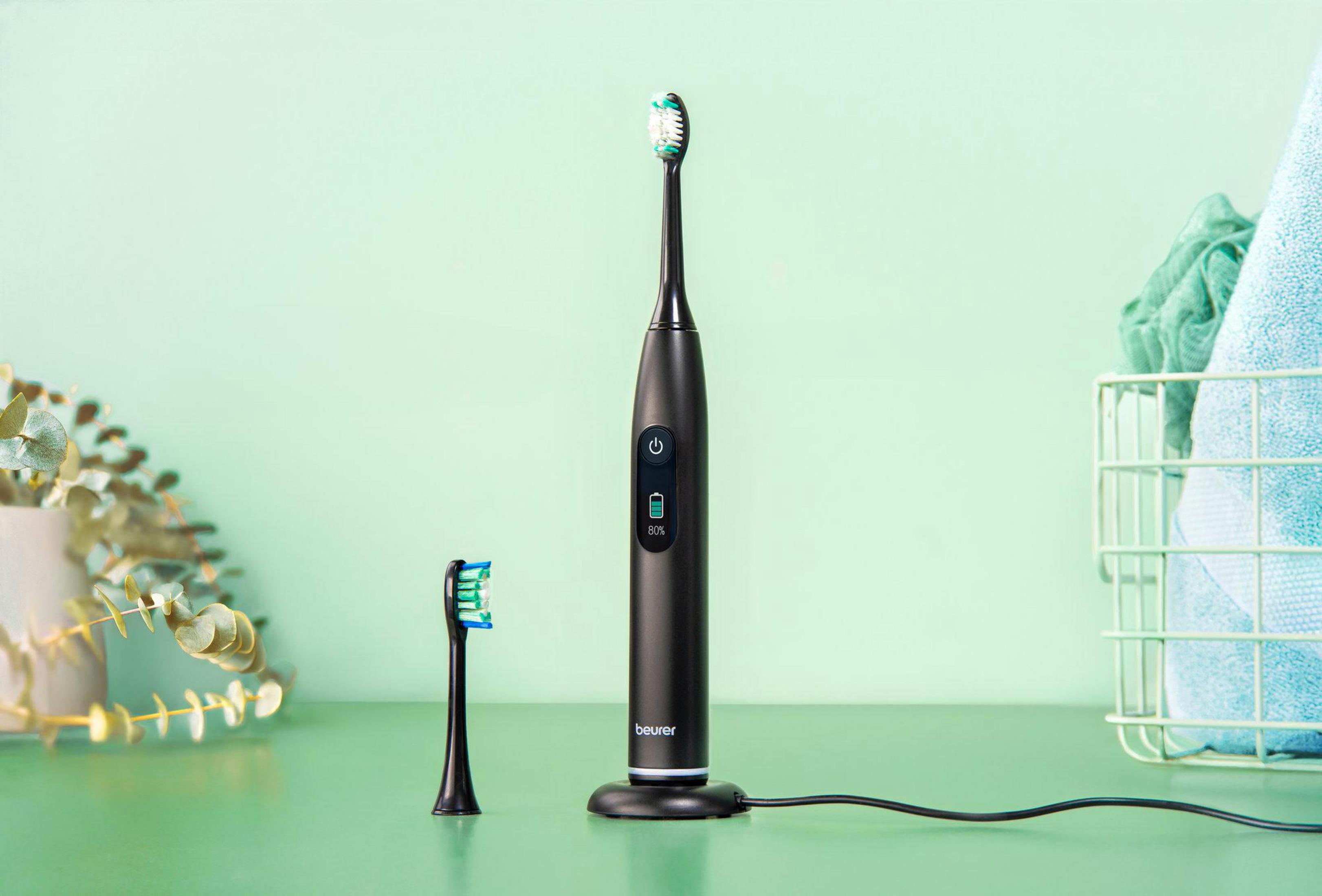 Black electric toothbrush with charging base, spare head, and plants.