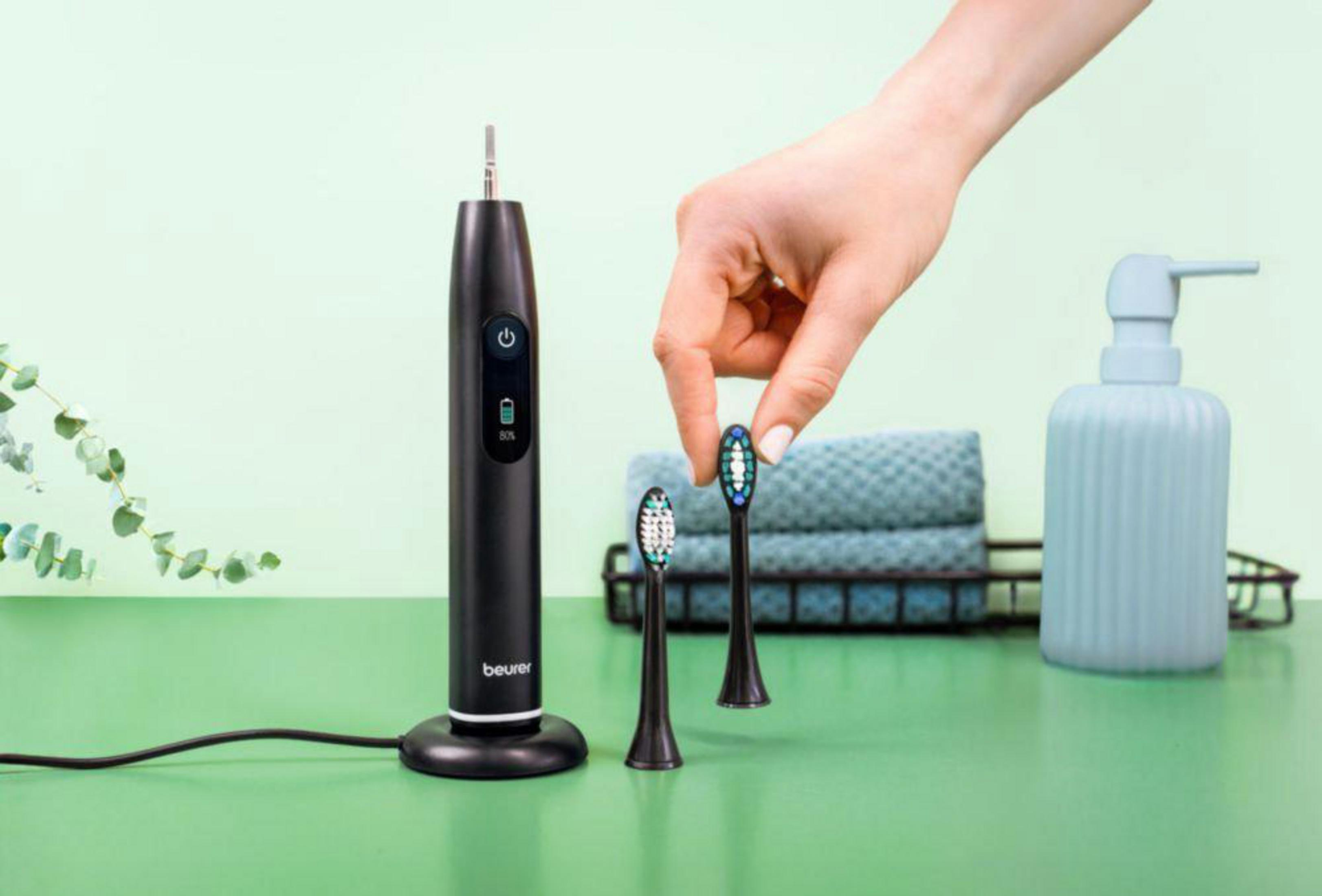 A black electric toothbrush with charging base, two brush heads, towels, and a soap dispenser.