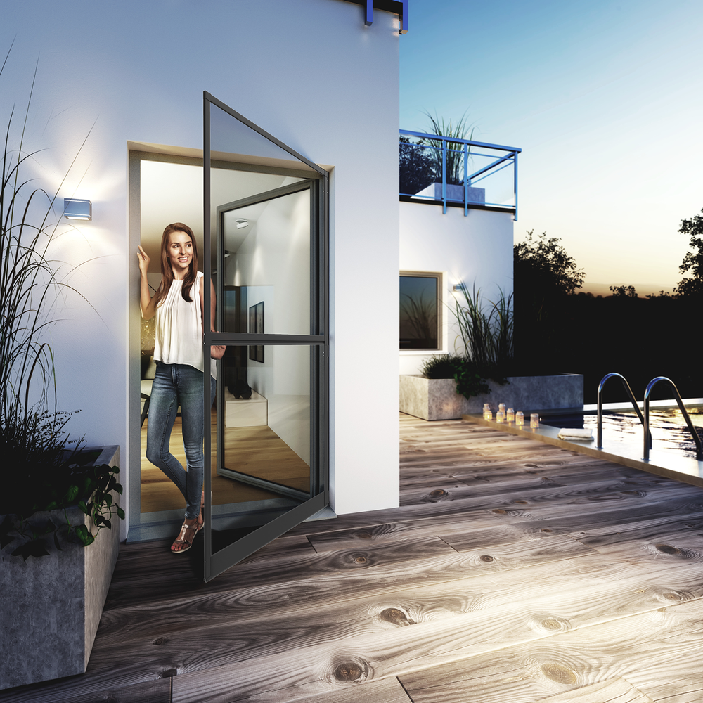 Frau in weißer Bluse steht in offener Glastür, Pool und Holzterrasse im Abendlicht.