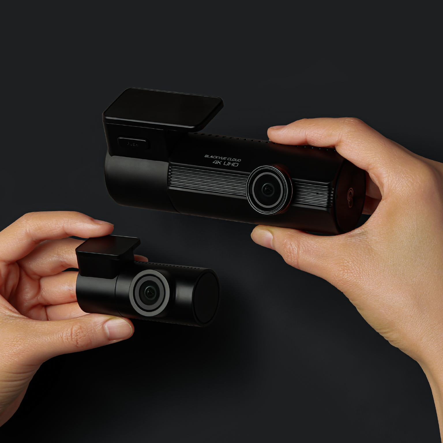 Hands hold two black dashcams against a dark background.