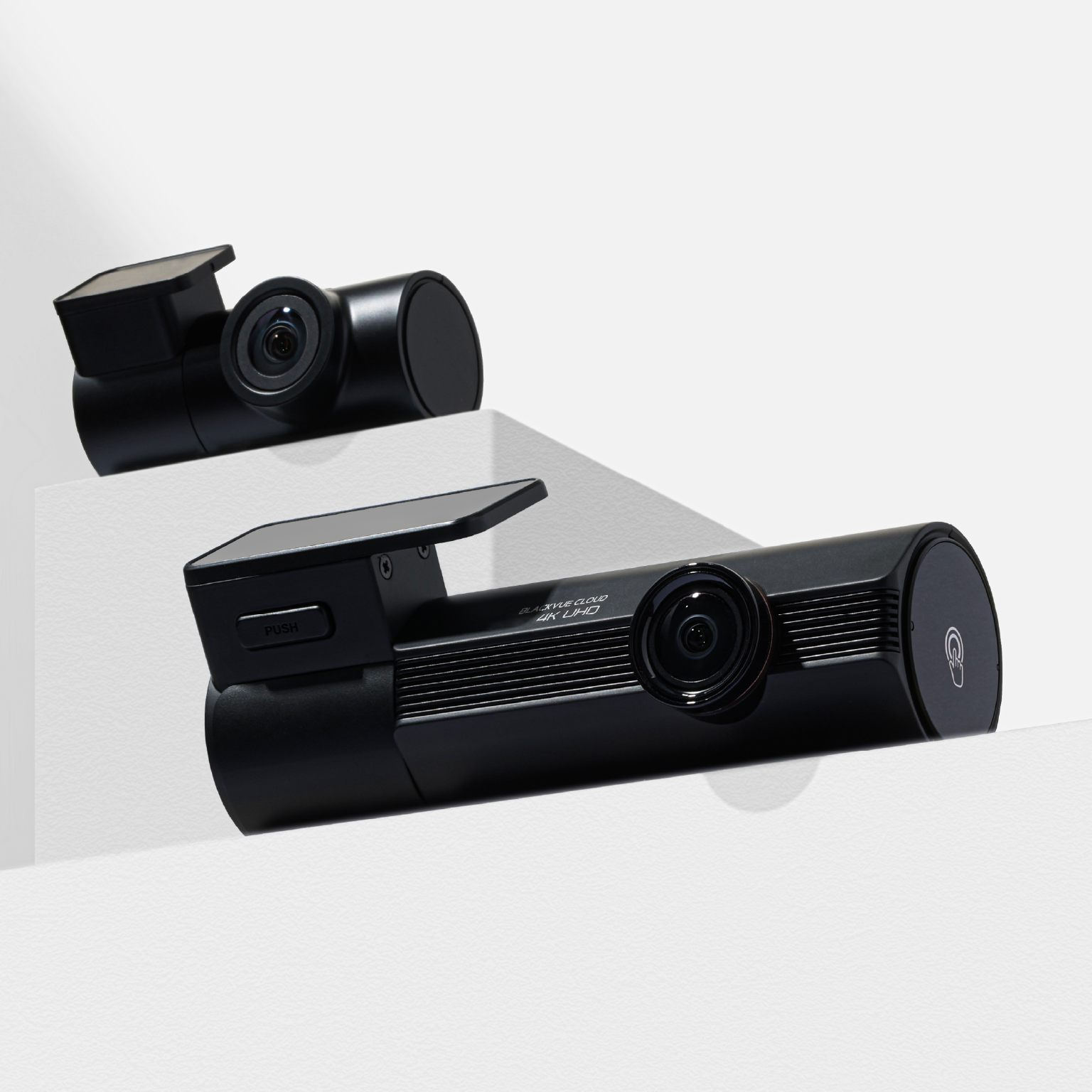 Two black dashcams on white surfaces, one in focus.