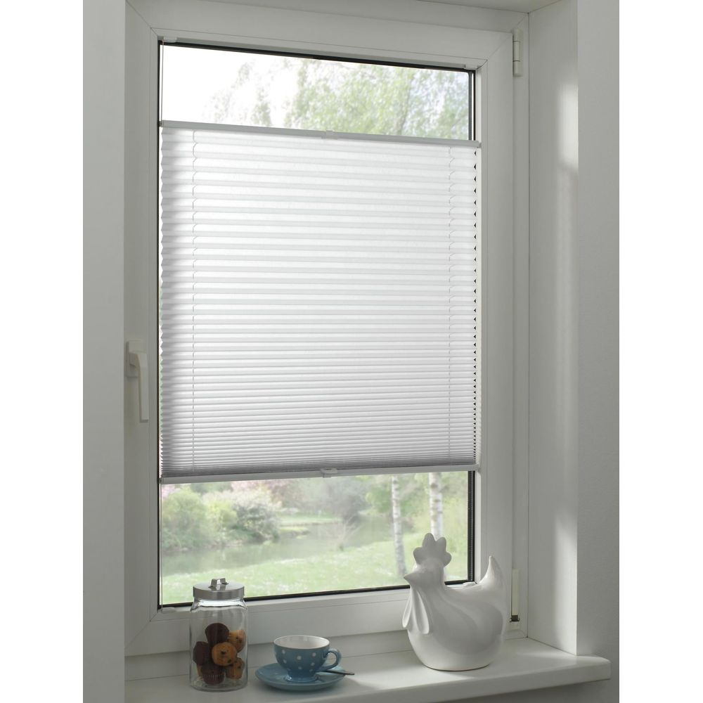 Weiße Plissees an einem Fenster mit einem Keksglaß, einer Teetasse und einer Hühnerfigur.