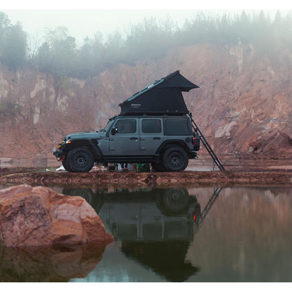 Grauer Jeep mit Dachzelt am Seeufer bei nebligem Wetter.