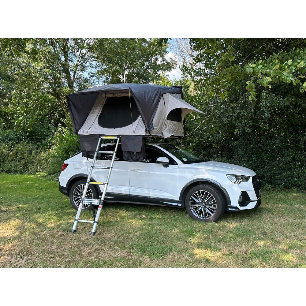 Auto bianca con tenda da tetto e scala, parcheggiata sull'erba con alberi.