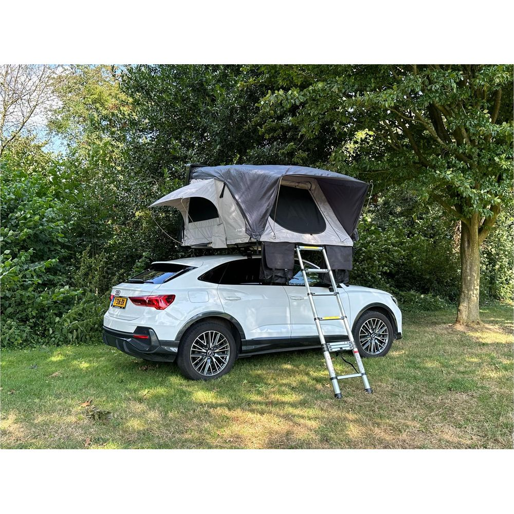 Un'auto bianca con tenda da tetto e scala sull'erba vicino agli alberi.