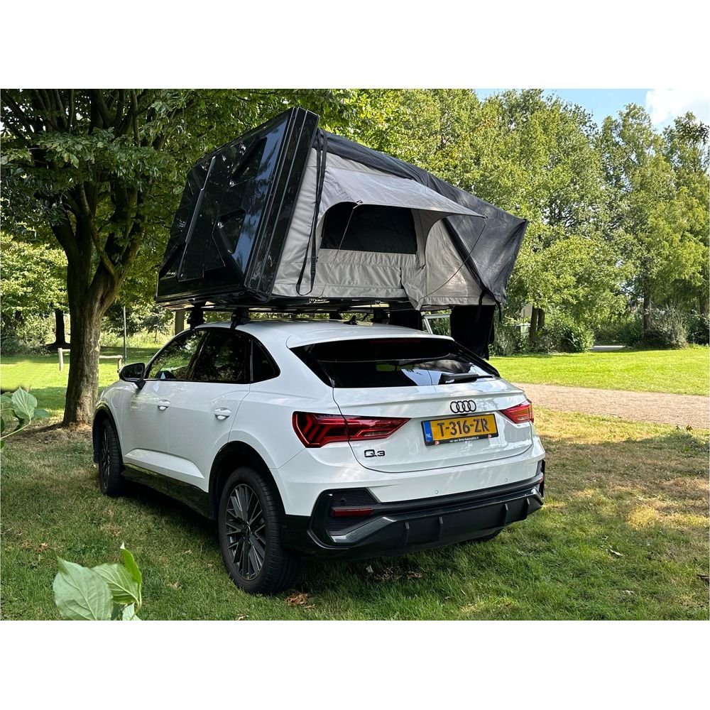 Una Audi Q3 bianca con tenda da tetto è parcheggiata su un prato vicino agli alberi.