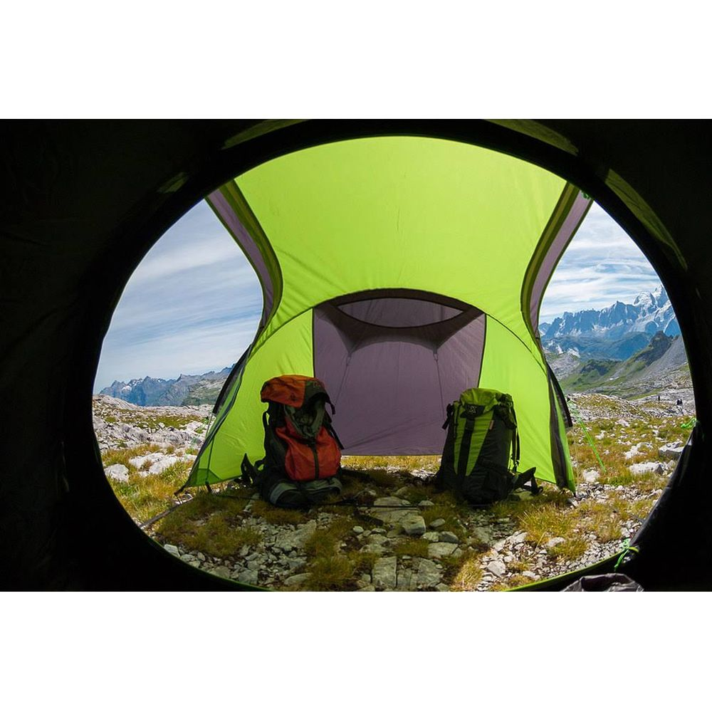 Due zaini davanti a una tenda aperta con paesaggio montano sullo sfondo.