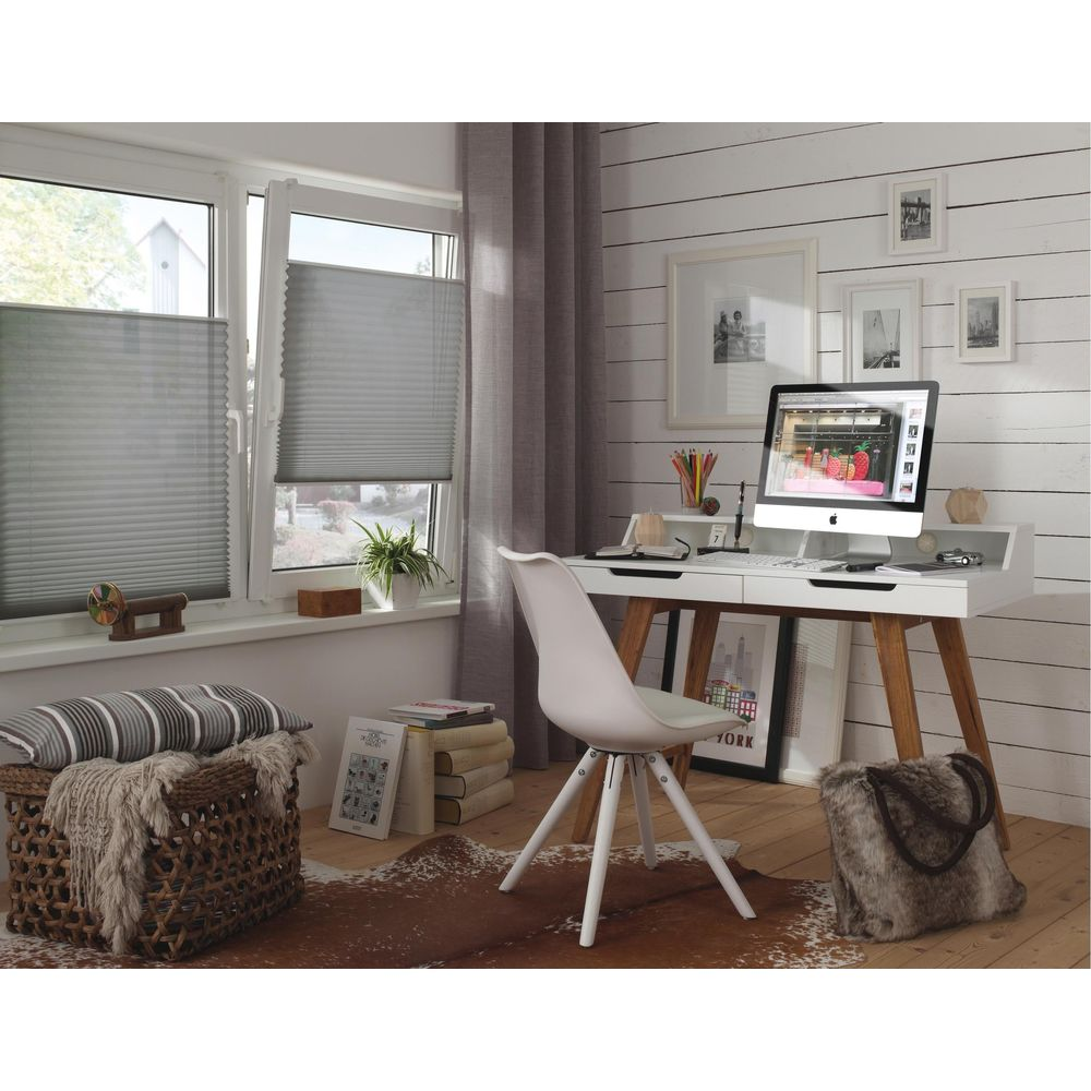 Ein Schreibtisch mit Computer, Stühlen, Korb und Decke vor einem Fenster.